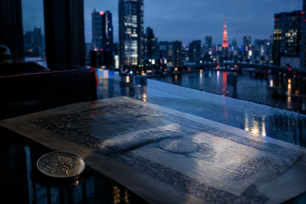 Tokyo skyline and a yen coin beside a Japanese bond certificate in blue-hour light