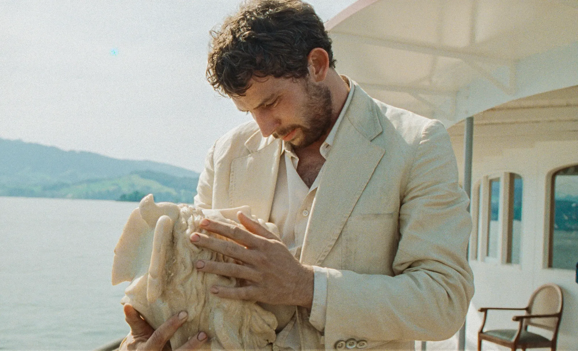 A still of Josh O'Connor in the movie La Chimera, looking absolutely so handsome in his white linen suit, cradling the head of a statue, and he looks so cute I just want to kiss him!!!!