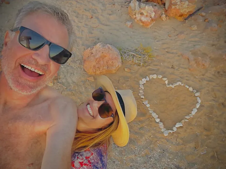 A horrific selfie taken by a shirtless Bill de Blasio, with him and his ex-girlfriend Nomiki smiling at the camera on a beach, and behind them is a heart made out of little rocks. They look deeply insane, and Bill de Blasio is surprisingly scrawnier than I expected