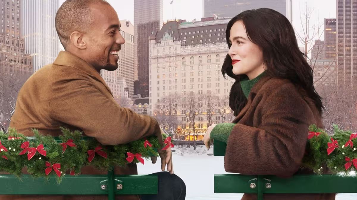 Kendrick Sampson and Zoey Deutch sit smiling at each other on festooned park benches in the snow