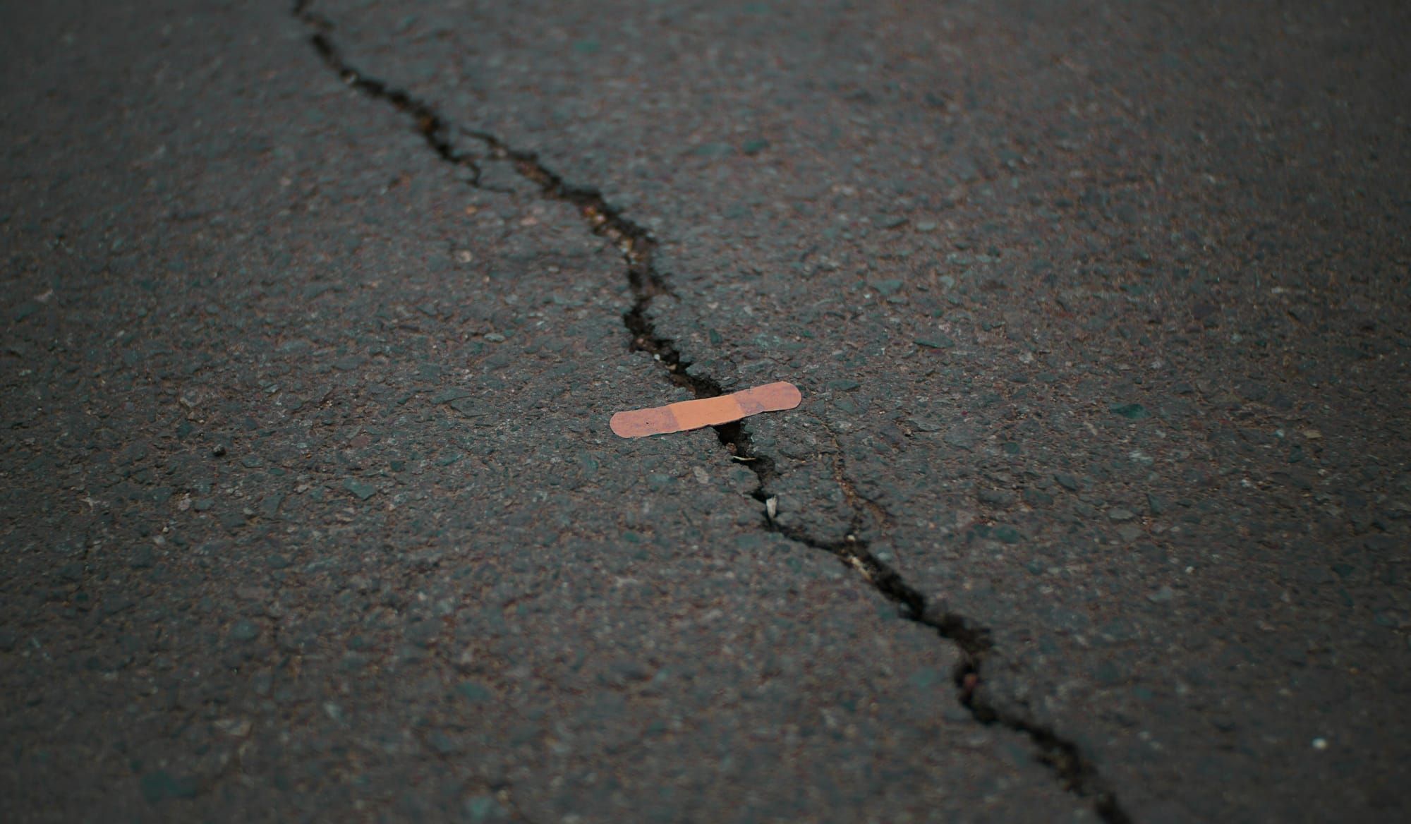 A crack in asphalt with a sticking plaster over it