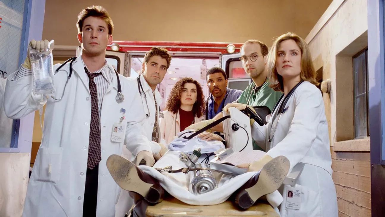 John Carter, Doug Ross, Carol Hathaway, Peter Benton, Mark Greene, and Susan Lewis stand dramatically around a patient on a gurney, covered by a sheet. 