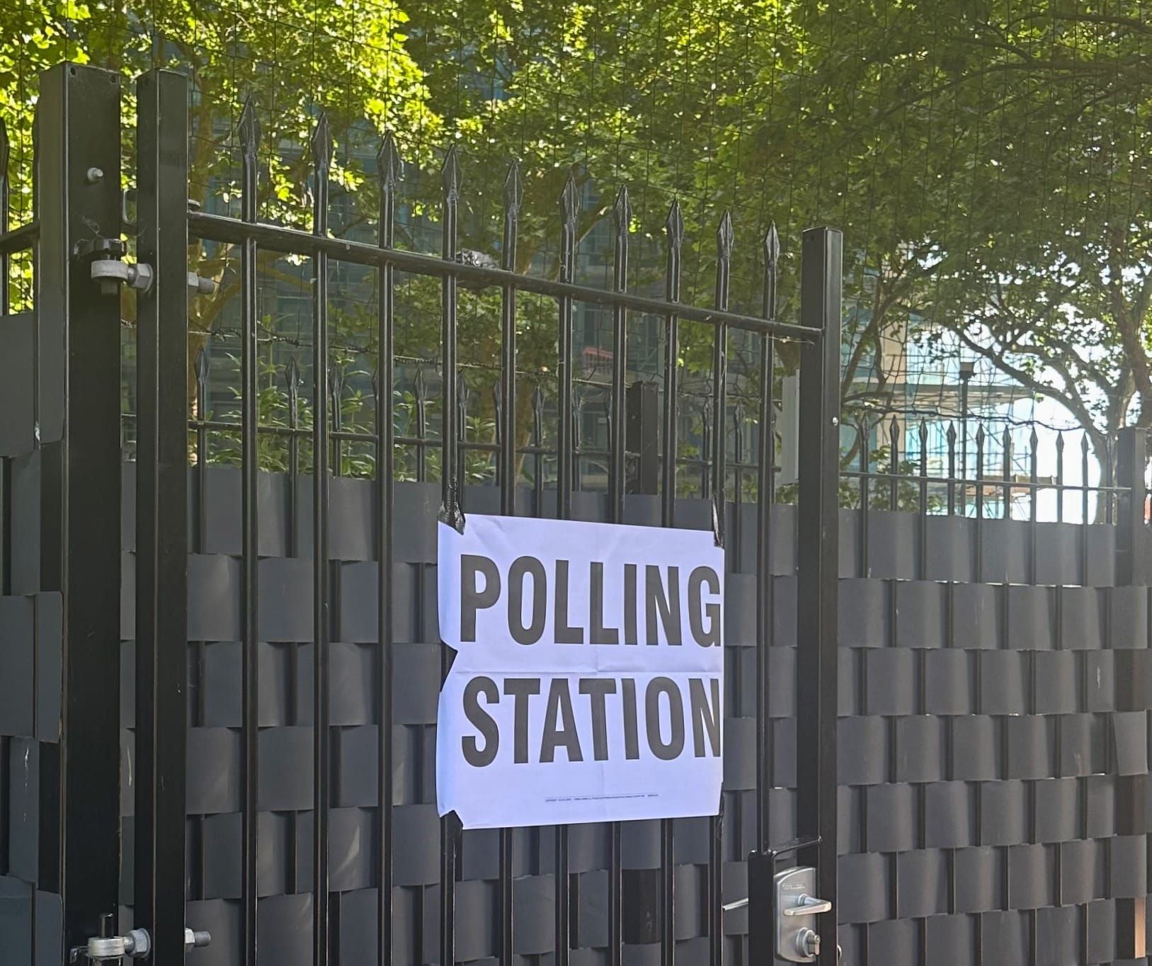 A sign reading "polling station" is taped to a black, wrought iron gate, with trees behind it