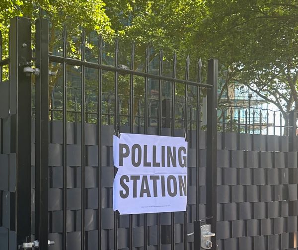 A sign reading "polling station" is taped to a black, wrought iron gate, with trees behind it