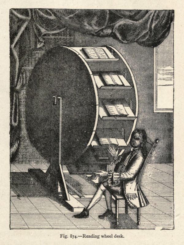 An elegant man  sits at a giant wheel with several shelves that each contain a book. 