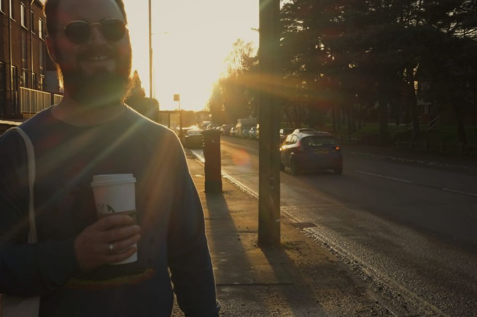 Man with a beard in his thirties wearing dark sunglasses holds a coffee in Norwich, Norfolk, 2022