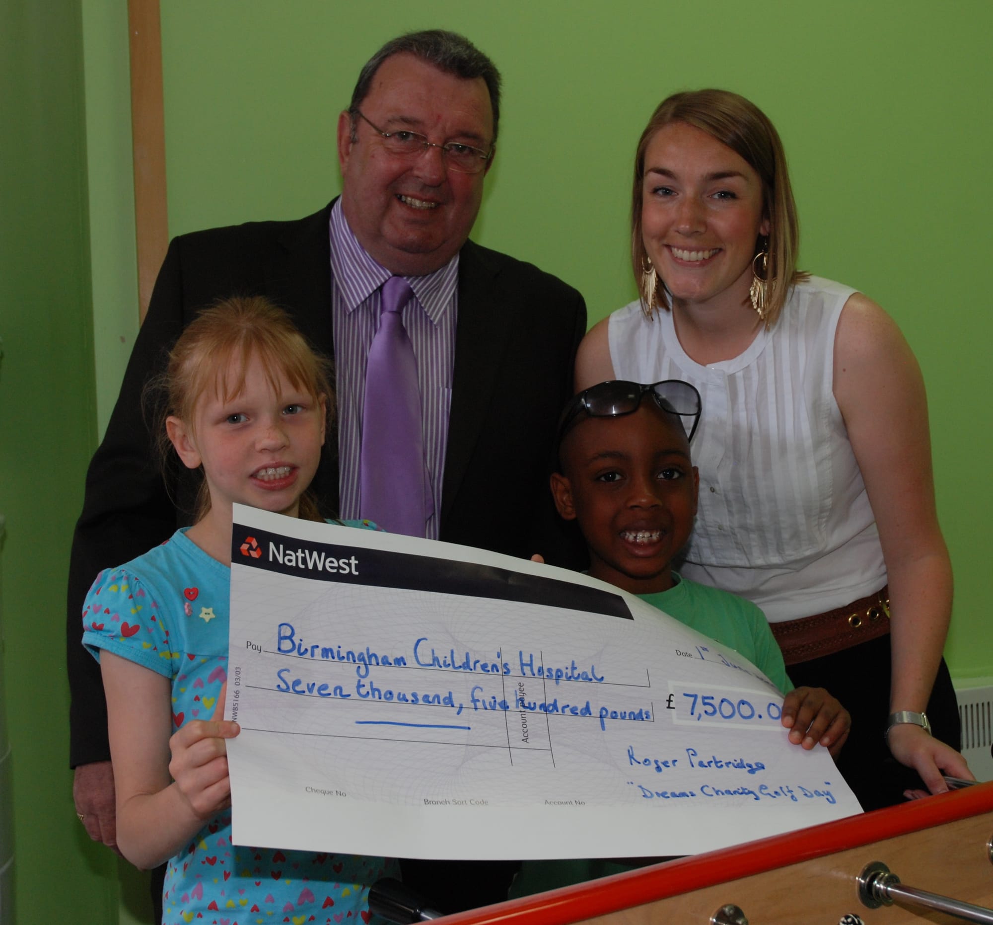 Roger Partridge presenting the cheque to Birmingham Children's Hospital Corporate Fundraising Manager Hynam Fidelis with young patients Believe and Dominique