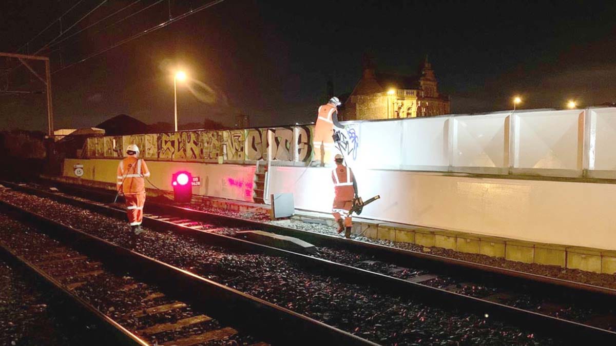 Crews cleaning graffiti from the side of the railway