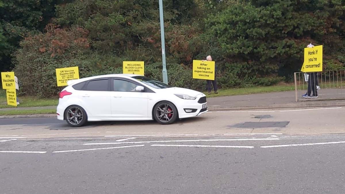 Vehicles driving past protesters outside The Friary School