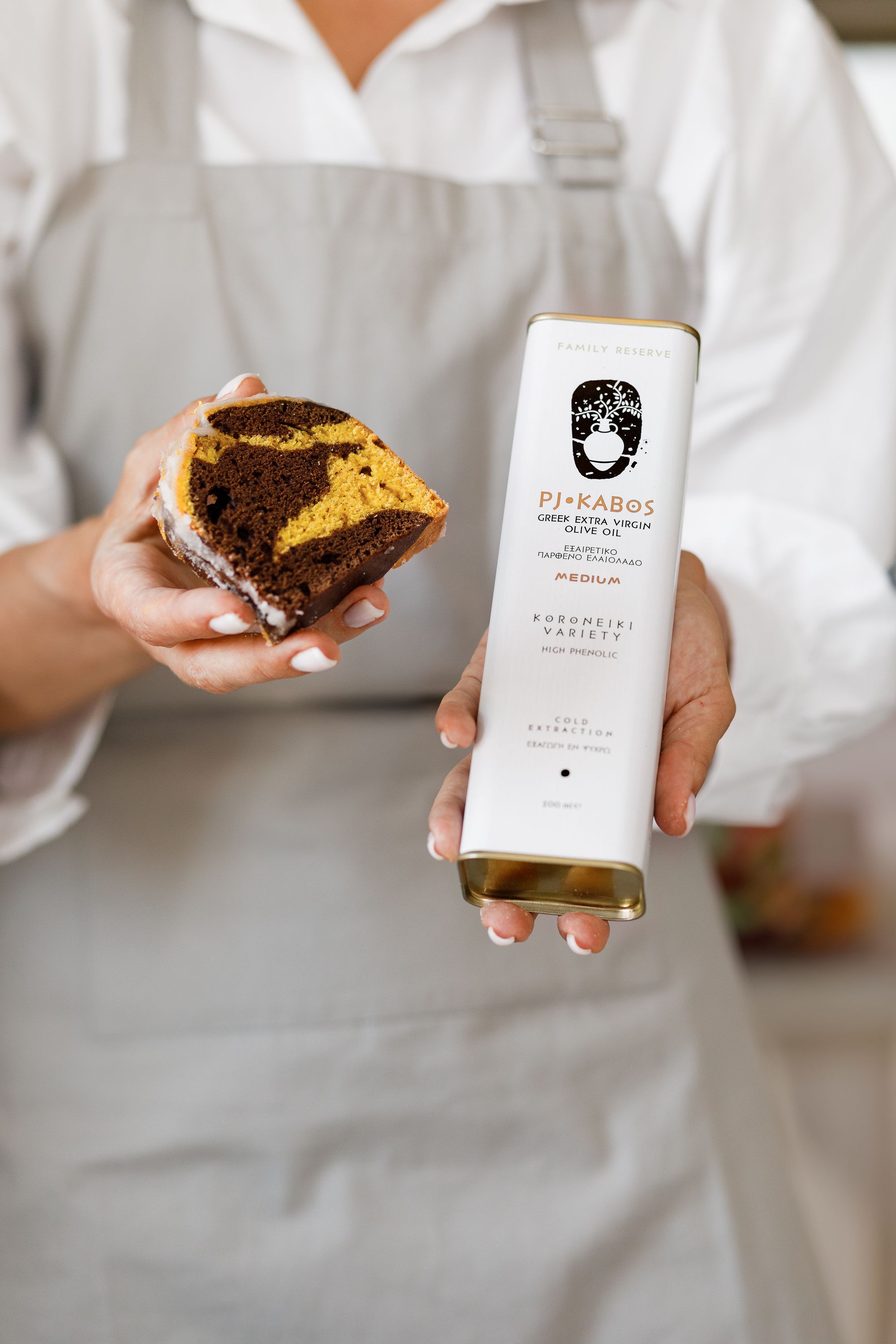 A woman holding a cake and a tin of high-quality, high in polyphenols PJ Kabos extra virgin olive oil