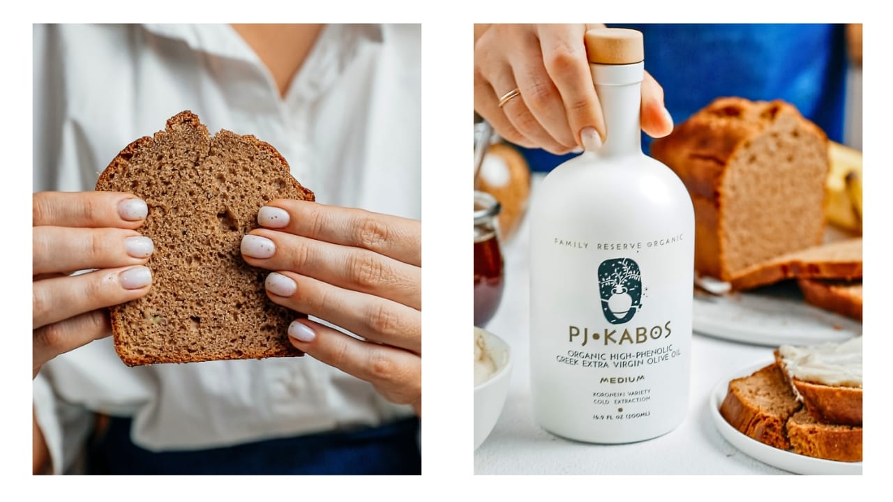 A woman holding a slice of banana bread and also indicating the PJ Kabos bottle of high-phenolic EVOO she used to make the bread.