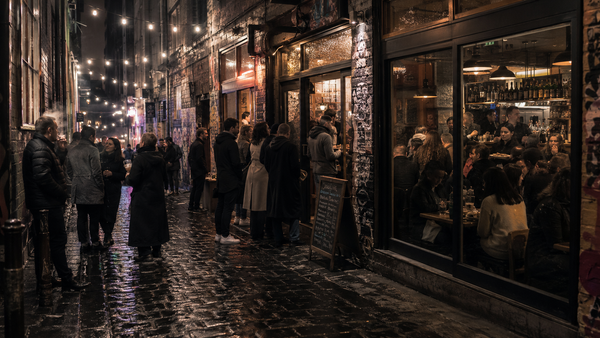 A packed Melbourne laneway at night with people drinking outside a full bar under string lights