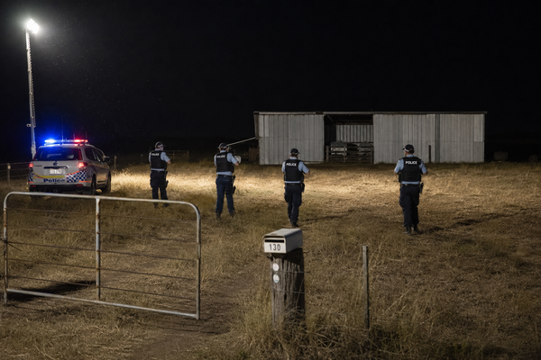 Queensland Police officers advancing across a floodlit rural paddock towards a shed at night