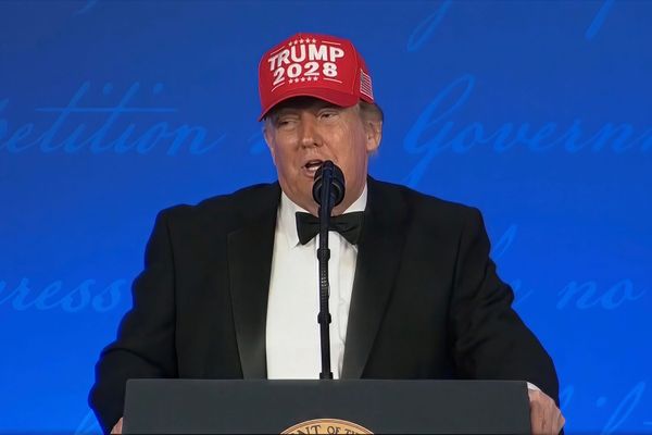 Donald Trump in a tuxedo and a red Trump 2028 cap speaking at a lectern