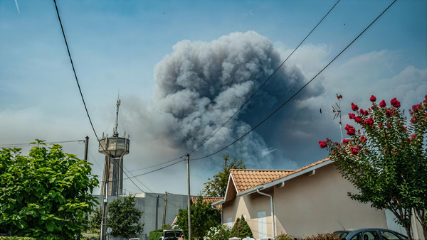 A towering column of wildfire smoke rising behind houses in southwest France
