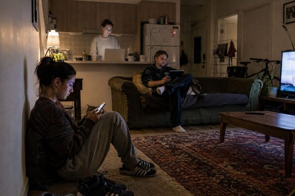 Three housemates in a share house at night, each filling in a form on a different device