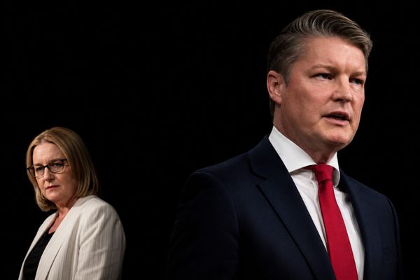 Ben Carroll in front, Jacinta Allan behind him turned away, both lit against black