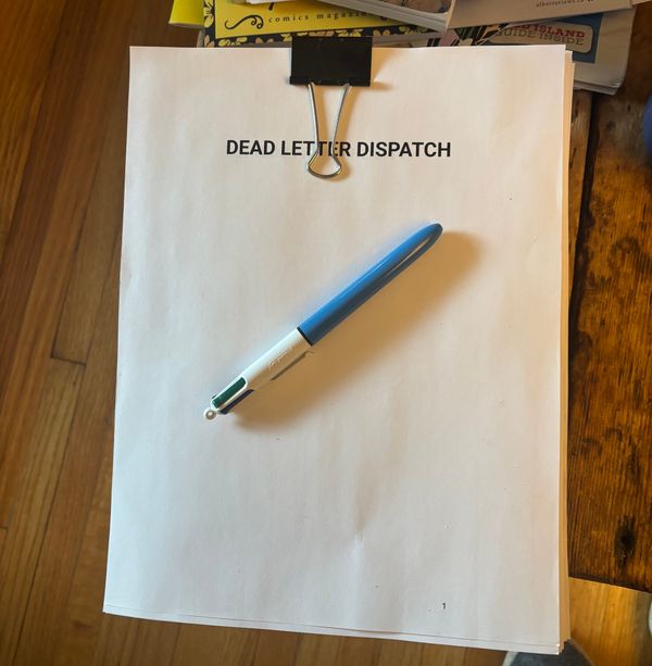 Printed pages from a manuscript on a wood table. The pages are held together by a a binder clip. The title of the manuscript is Dead Letter Dispatch. There is a Bic pen resting on top.