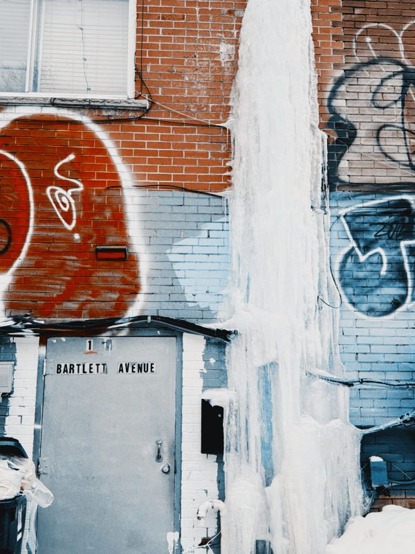 a brick wall covered in graffiti, with a tower of ice cascading down the face of it. 