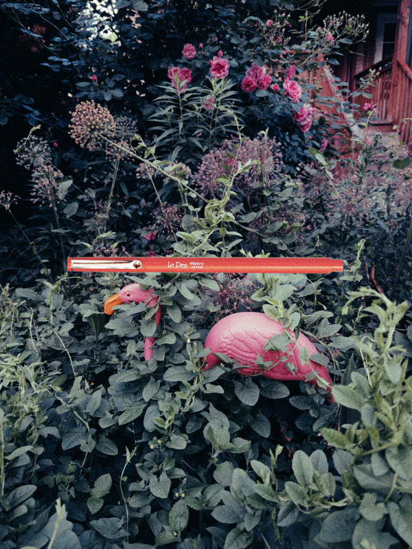 a plastic flamingo buried in a bunch of leaves and plants, and over it a red LePen