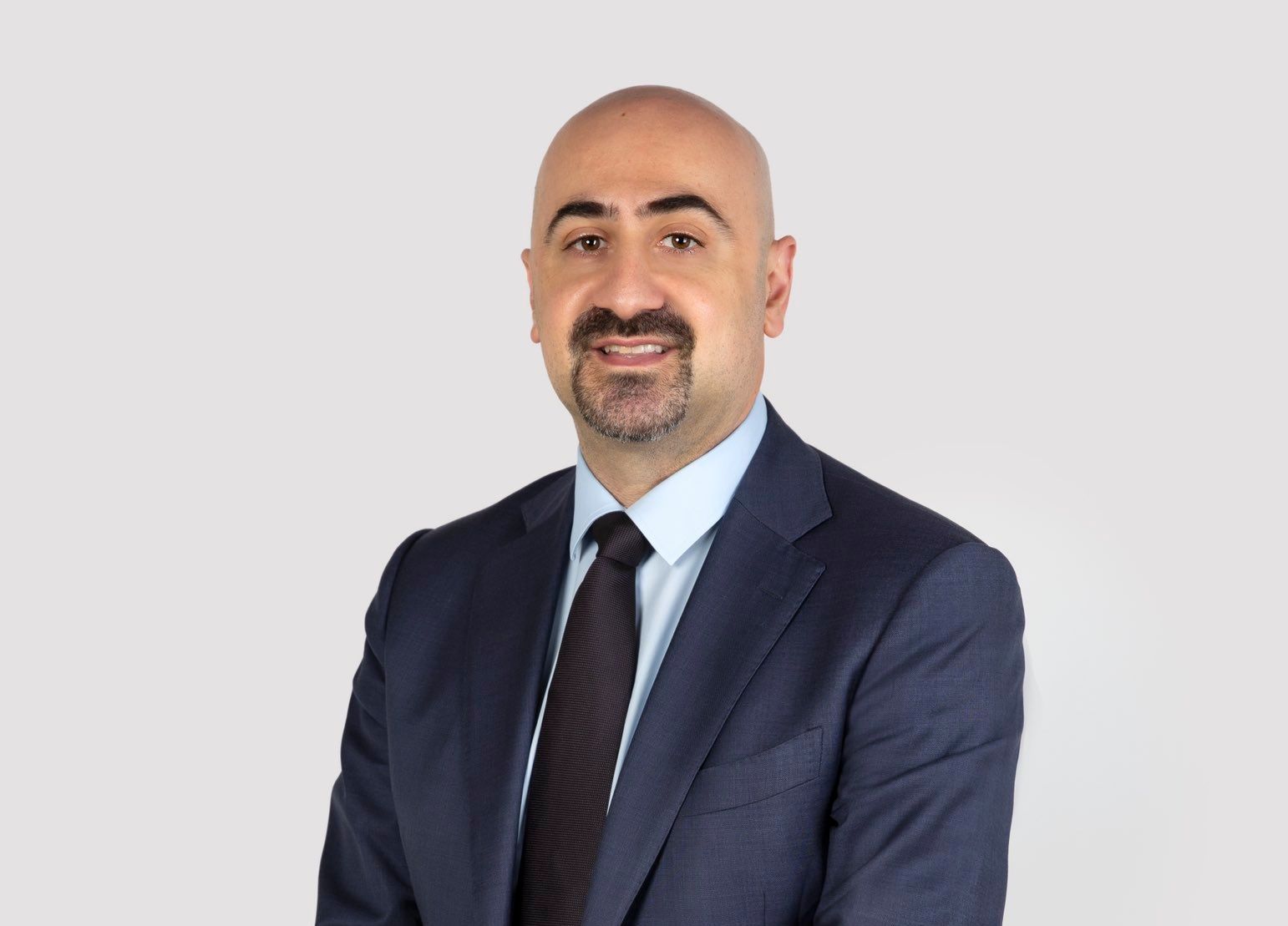 Photograph of Dr Joseph El-Khoury wearing a navy suit, sky blue shirt, and black tie, smiling into the camera
