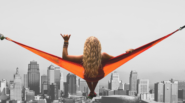 A woman is sitting in a hammock with her back to the camera, the hammock is hanging in the sky, a cityscape in the background