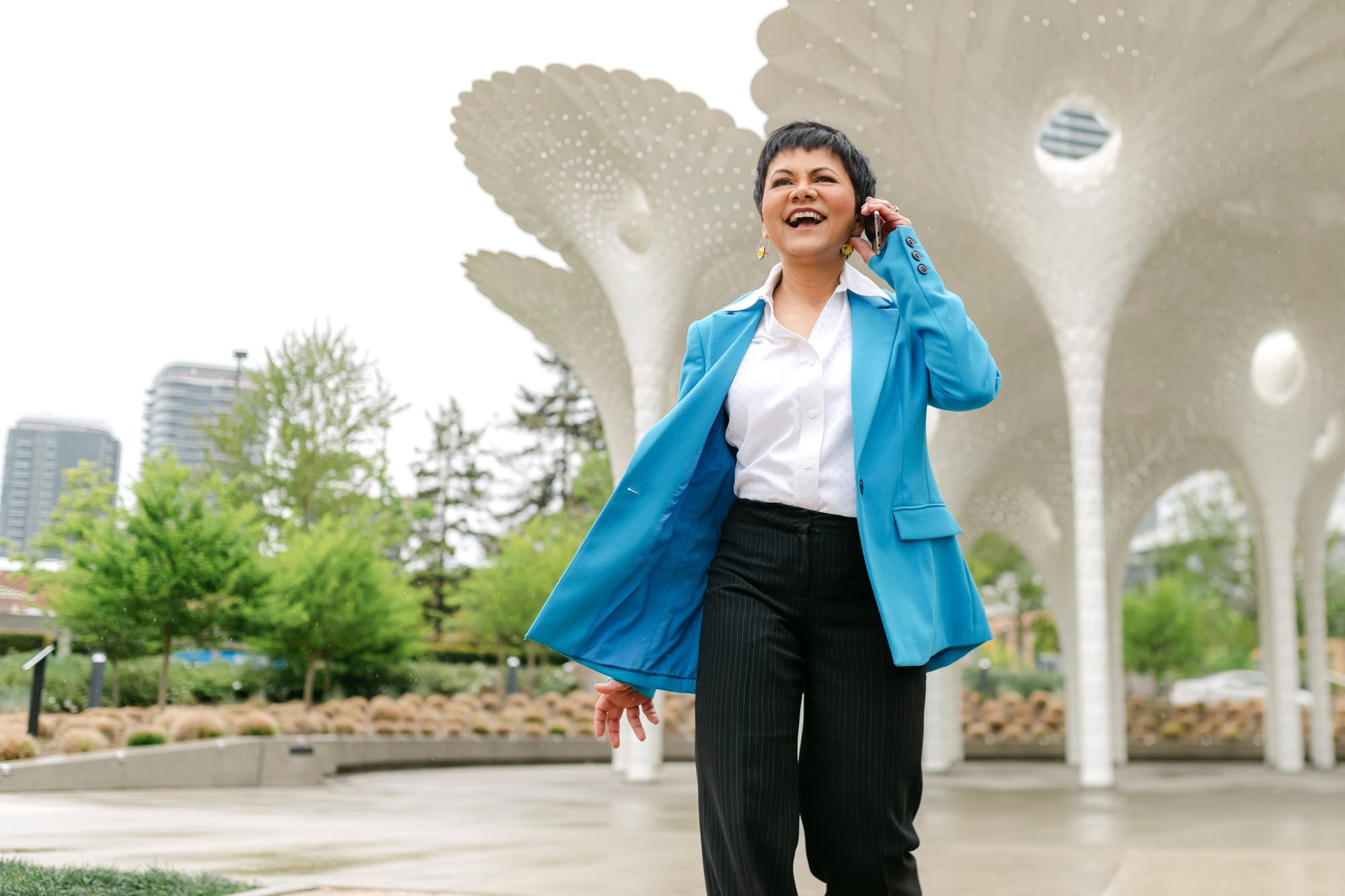 Consultant in a bright blue blazer laughing on a phone call outside a modern pavilion