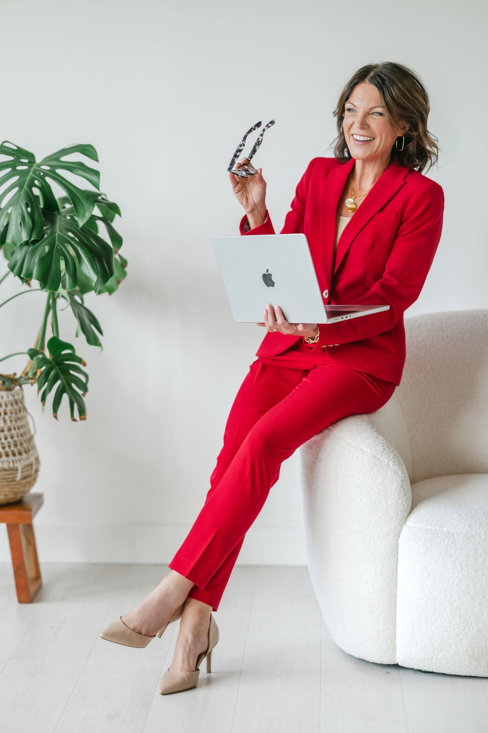 Executive in a red suit holding a laptop in a bright white studio