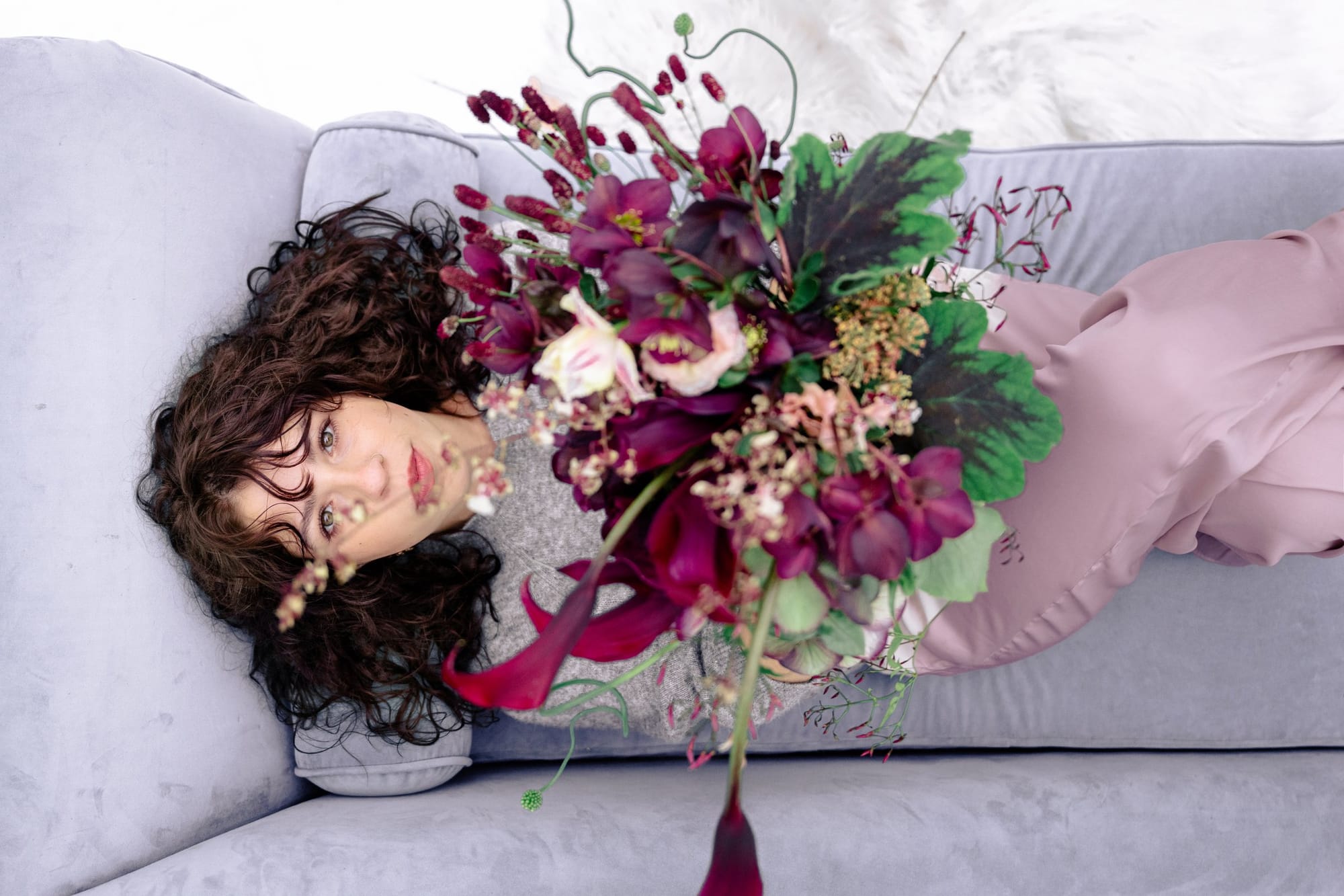 Florist reclining on a sofa with an armful of burgundy blooms