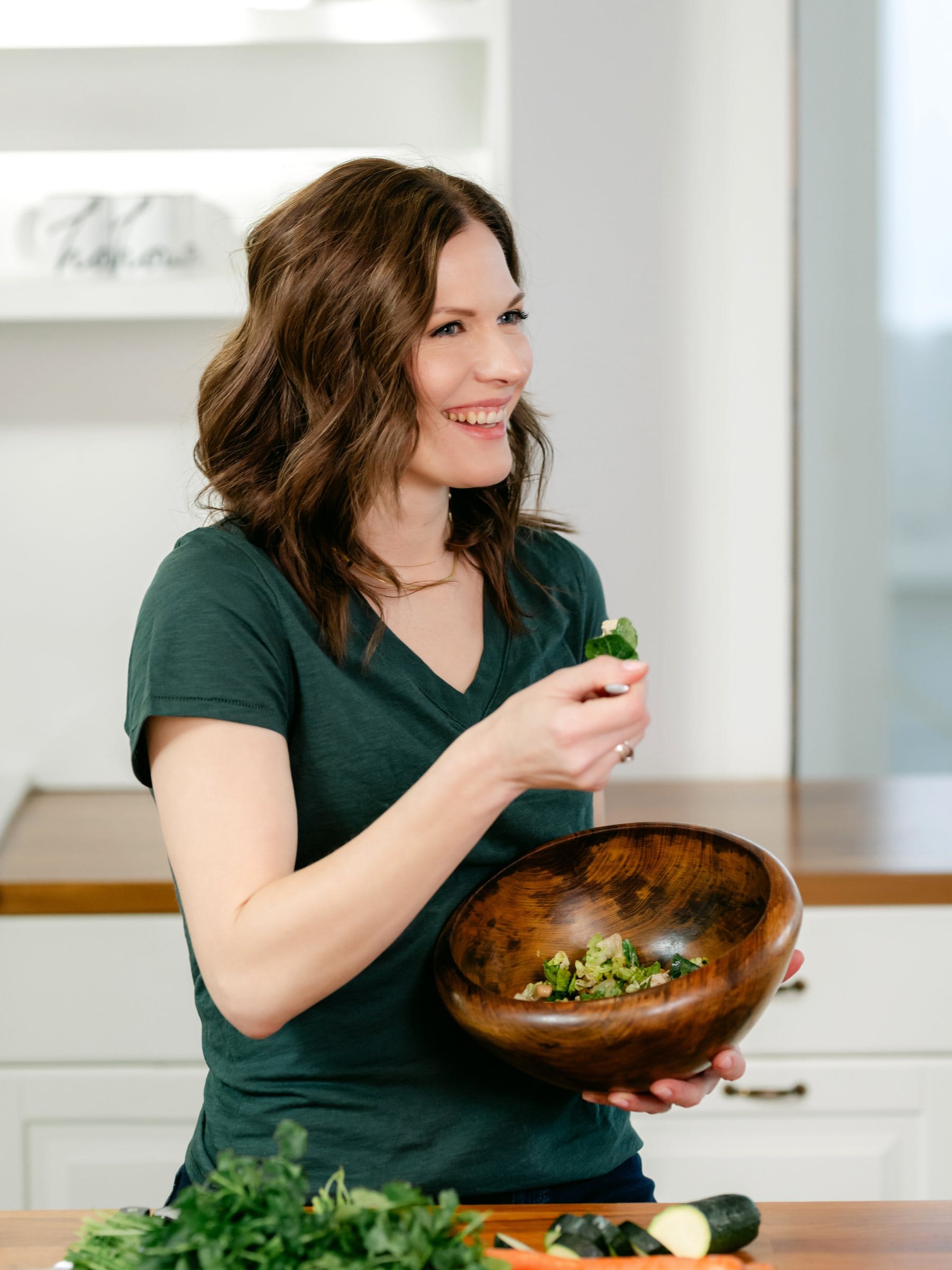 Nutritionist holding a wooden bowl of greens in her kitchen
