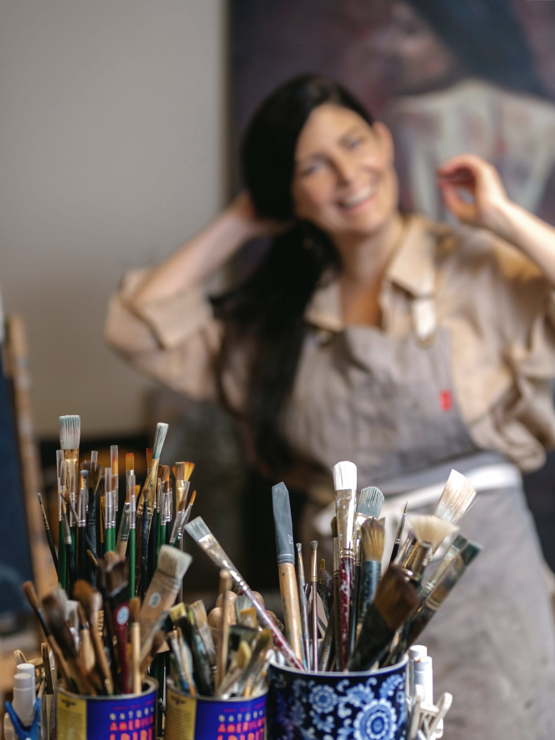 Painter smiling behind jars of brushes in her studio