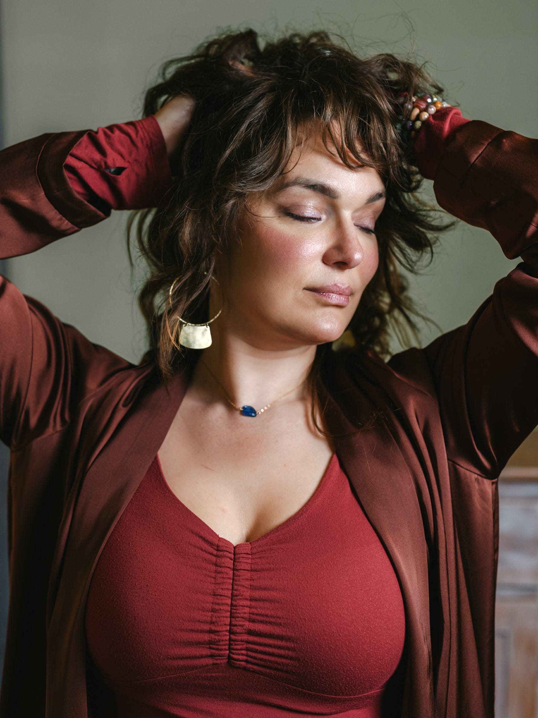 Woman in burgundy with her hands in her hair and eyes closed