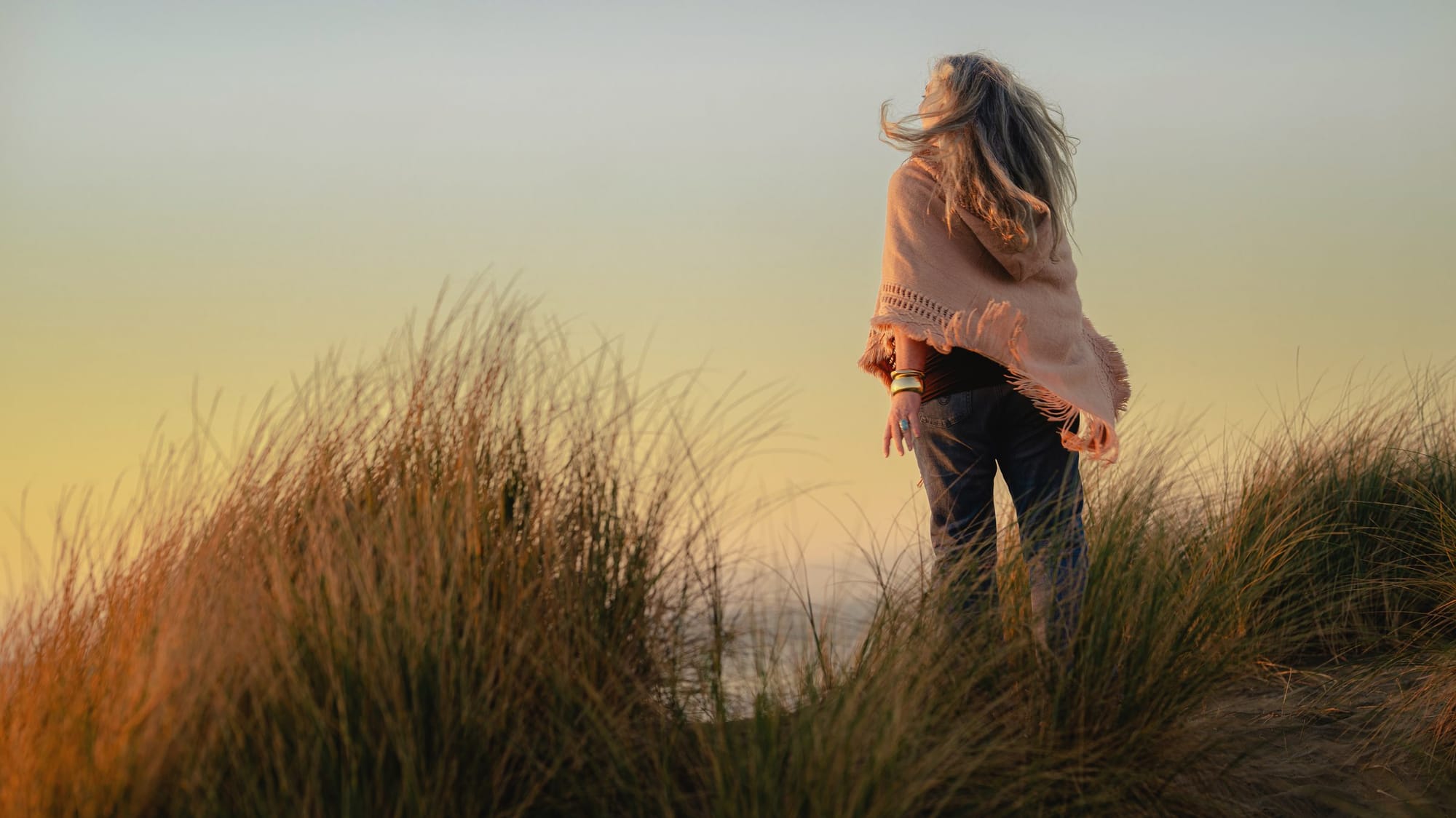 Woman walking through dune grass at golden hour