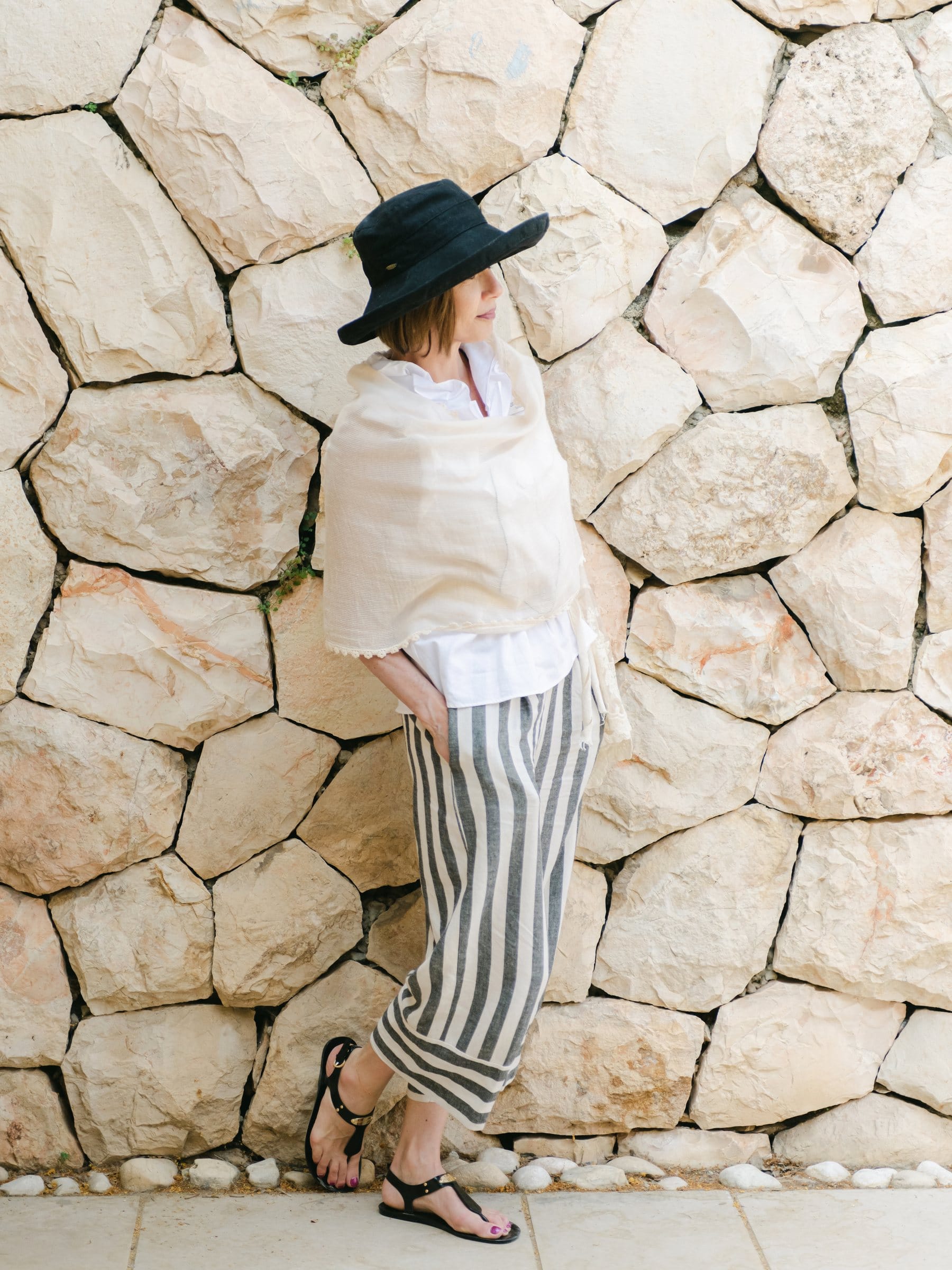 Woman in a wide-brim hat leaning against a pale stone wall