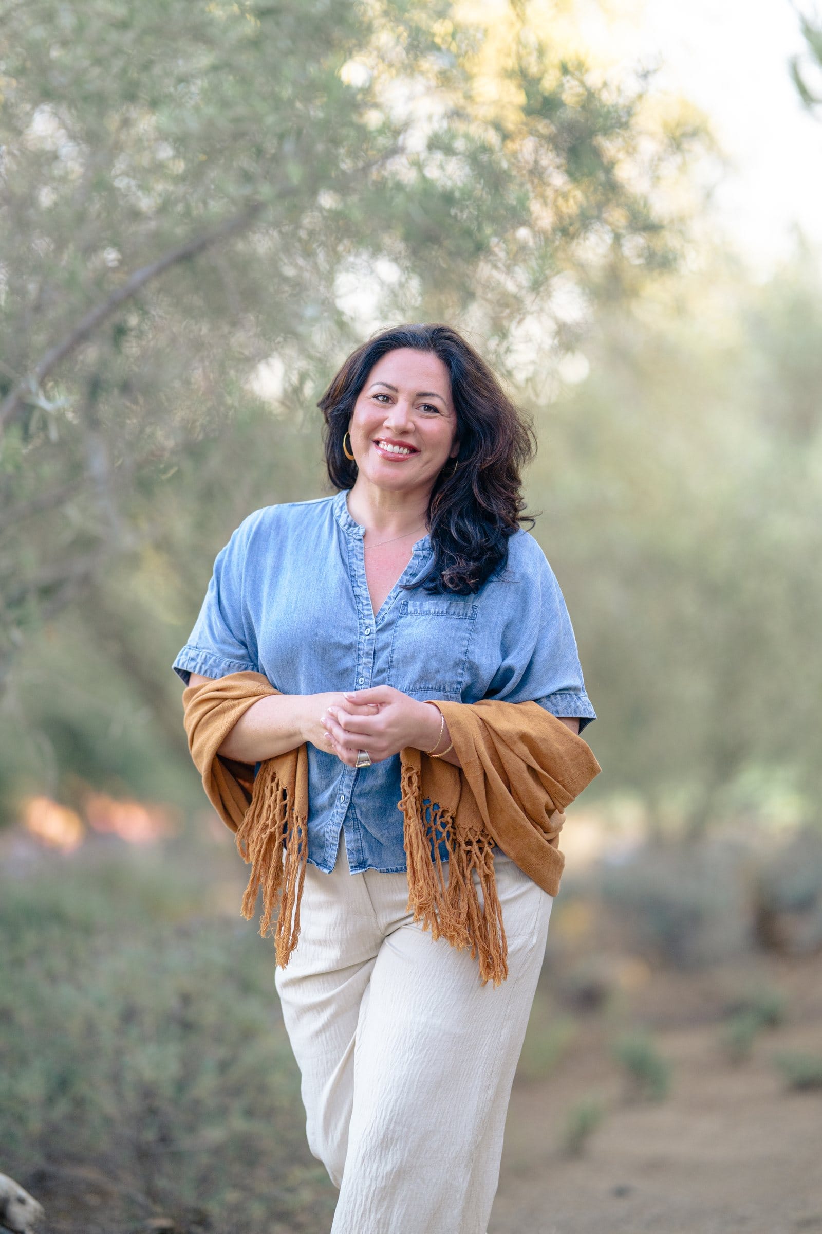 Smiling woman in a chambray shirt and fringed shawl in an olive grove