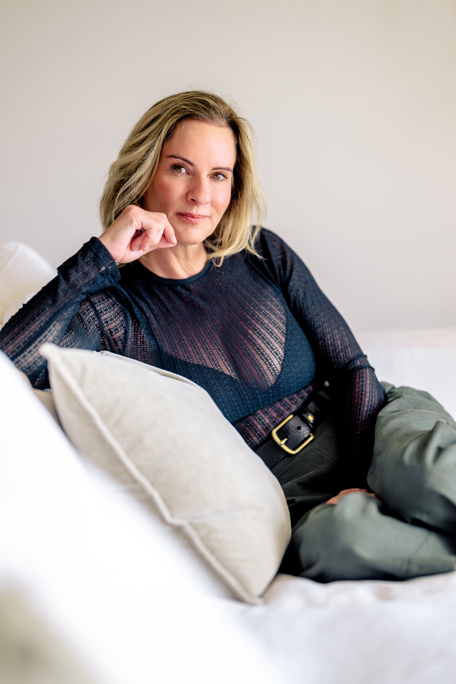 Woman in sheer navy resting her chin on her hand on a white sofa
