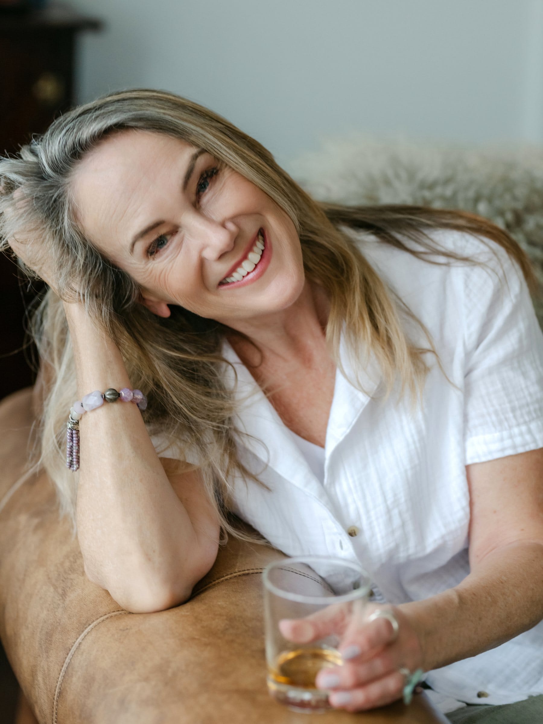 Woman with a drink leaning on a leather sofa, laughing