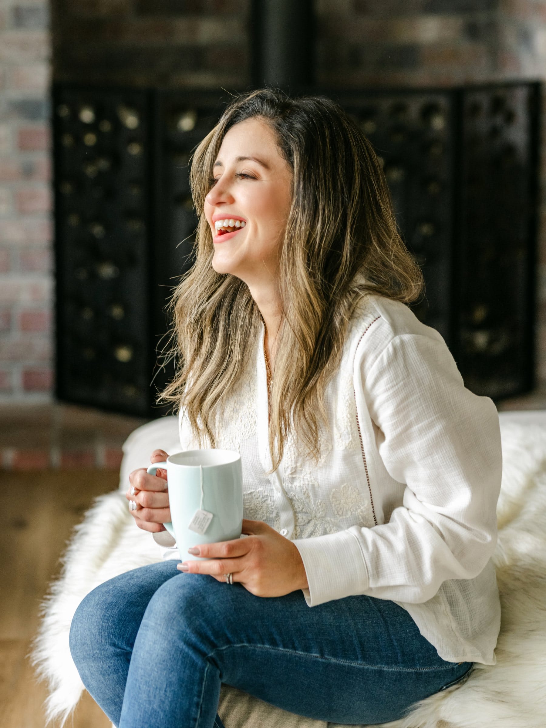 Woman laughing with a mug of tea on a sheepskin throw