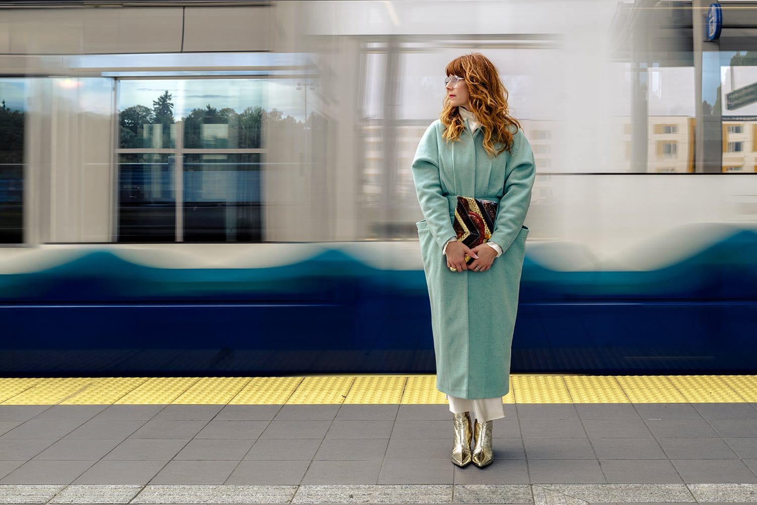 Woman in a mint coat on a subway platform as a train streaks past