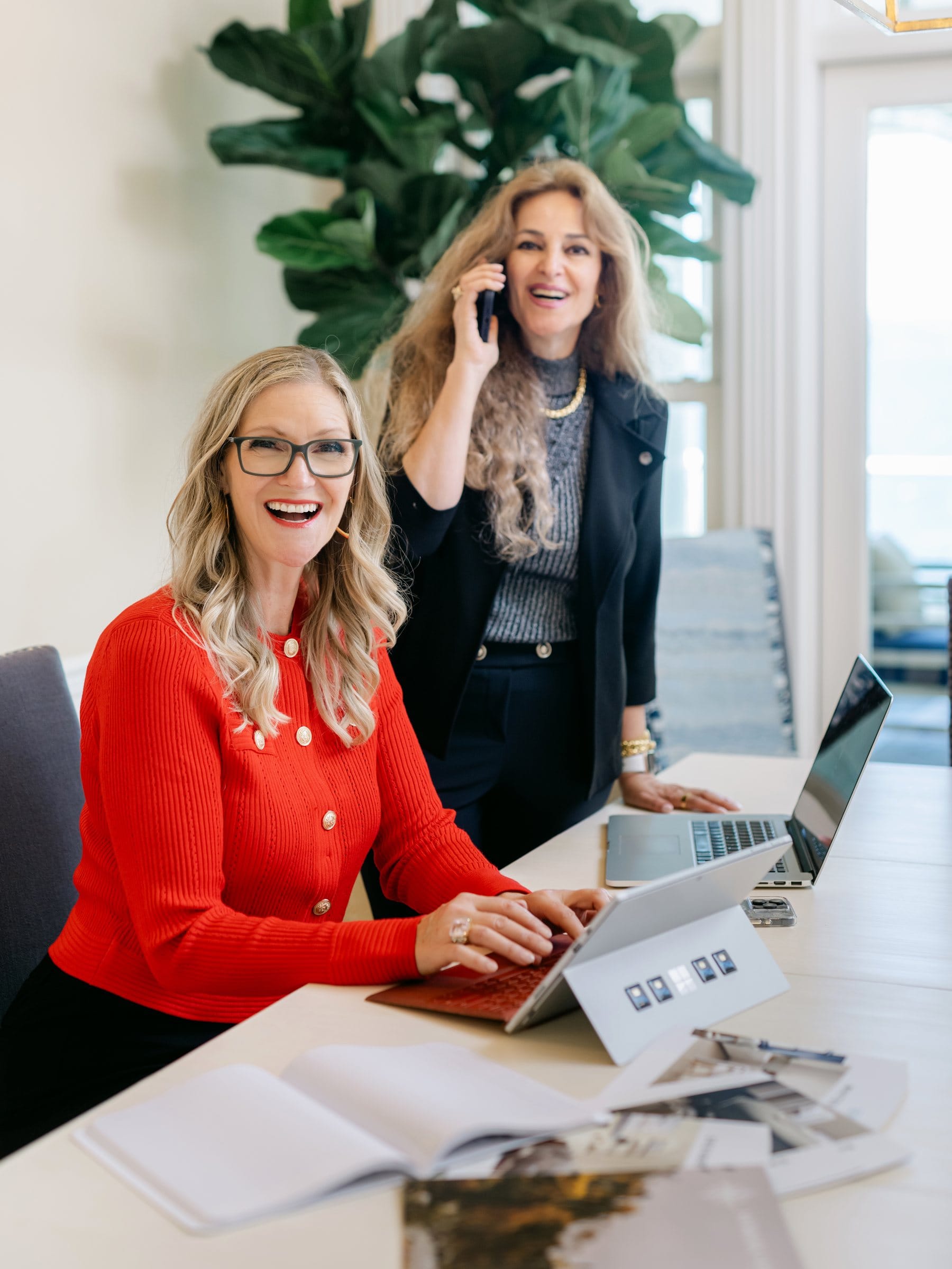 Two women working at a bright desk, one on the phone