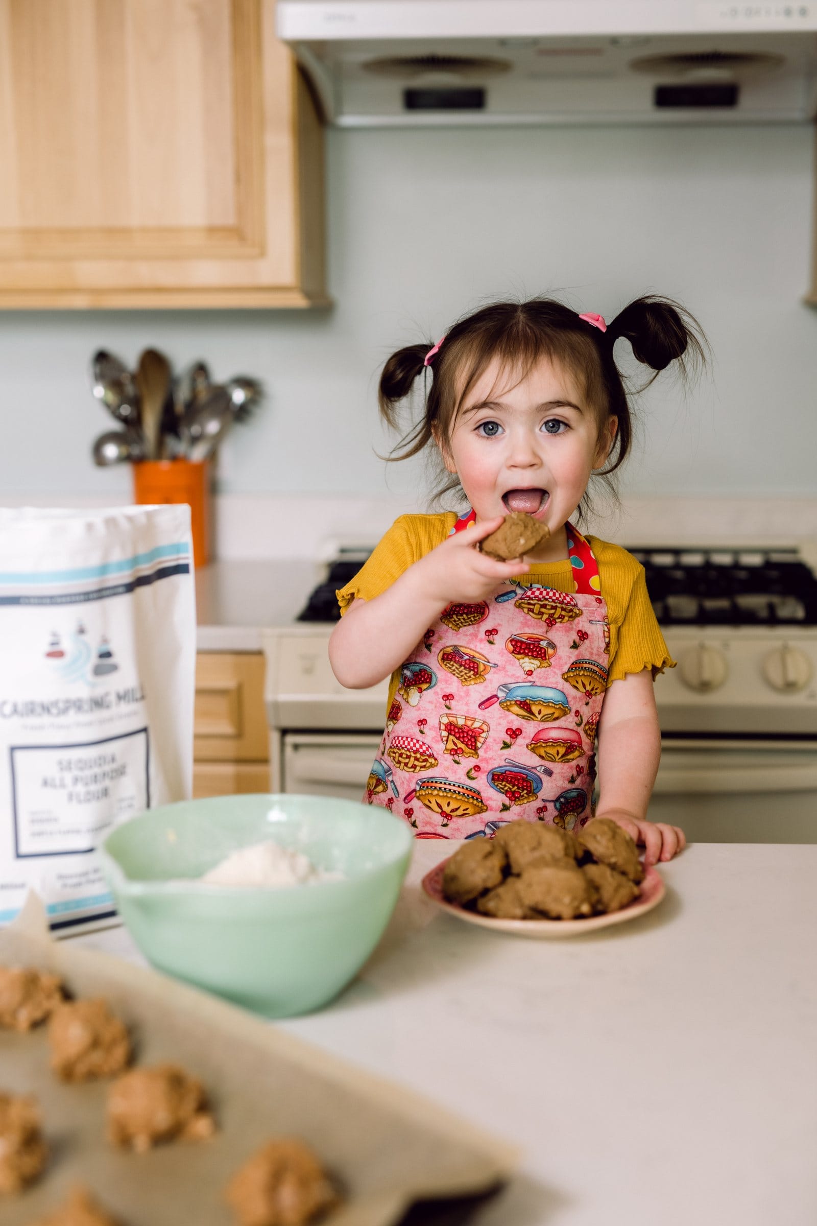 Toddler with pigtails sneaking cookie dough in the kitchen