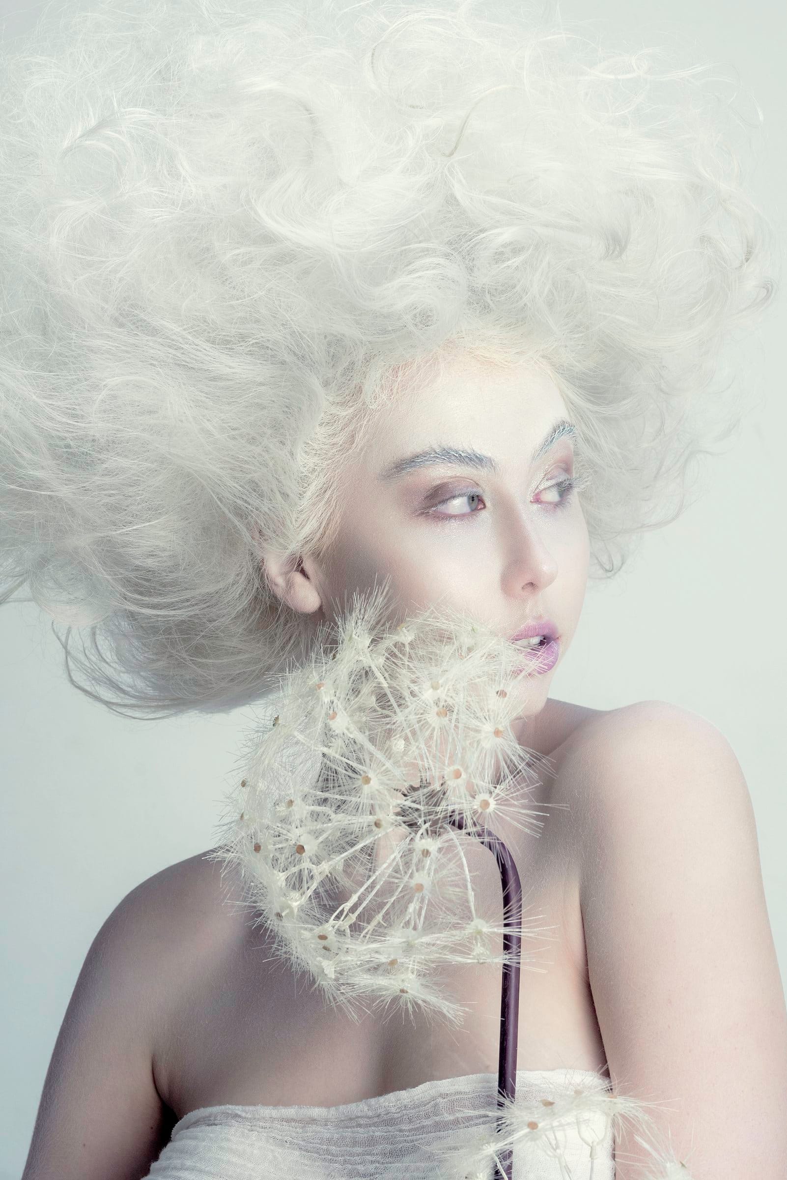 Ethereal editorial portrait with white sculpted hair and a dandelion