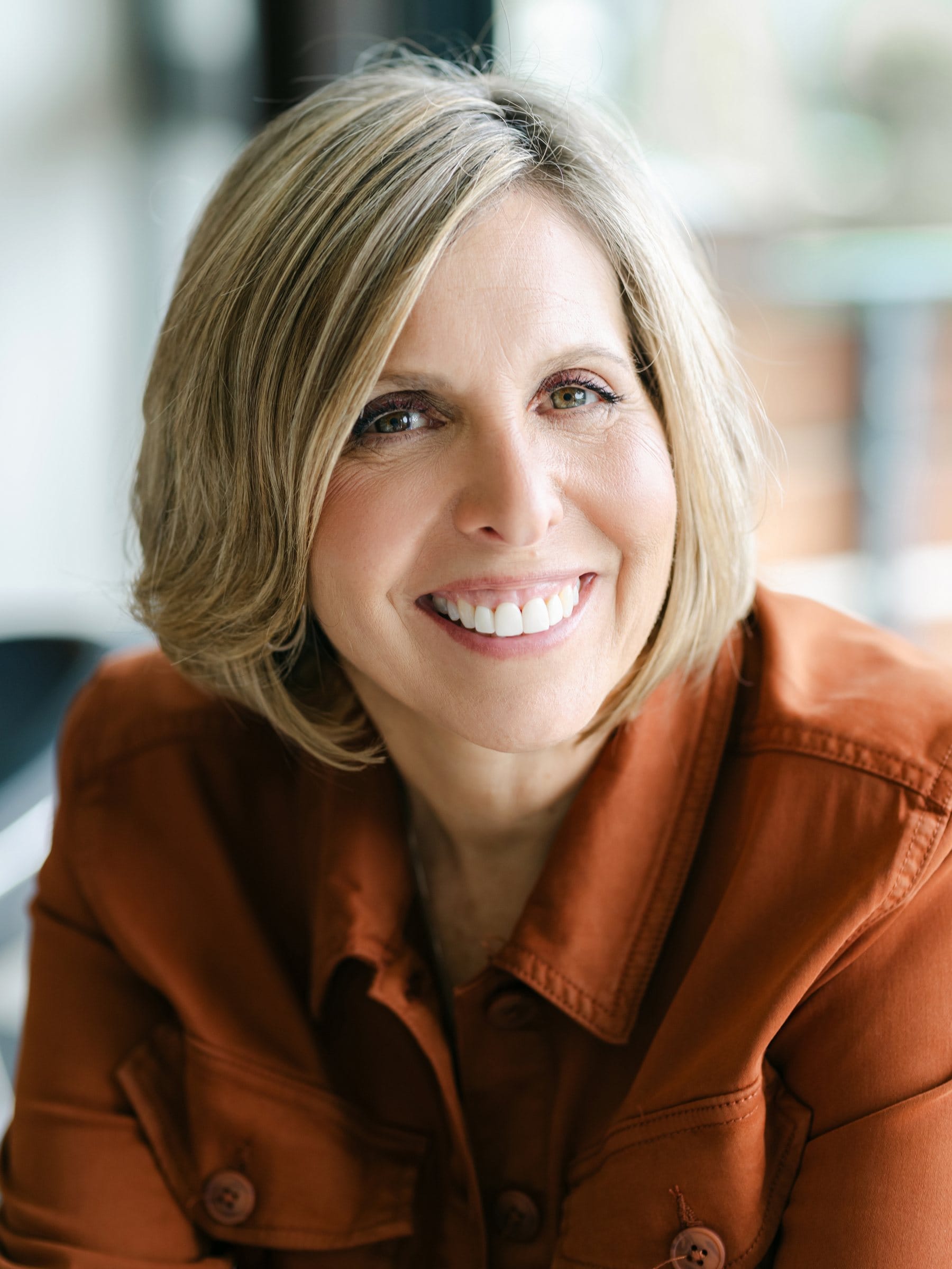 Close-up headshot of a smiling woman in a rust shirt