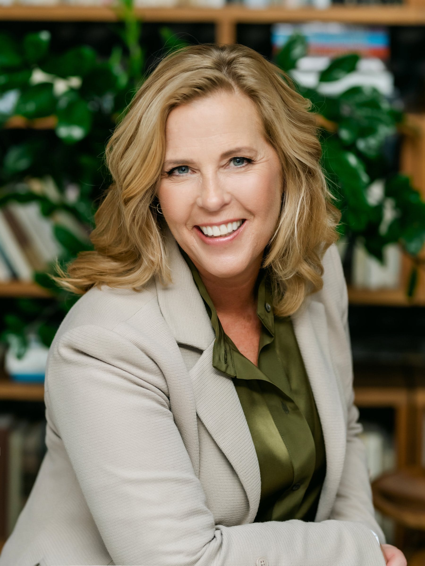 Smiling executive in a taupe blazer in front of her bookshelves