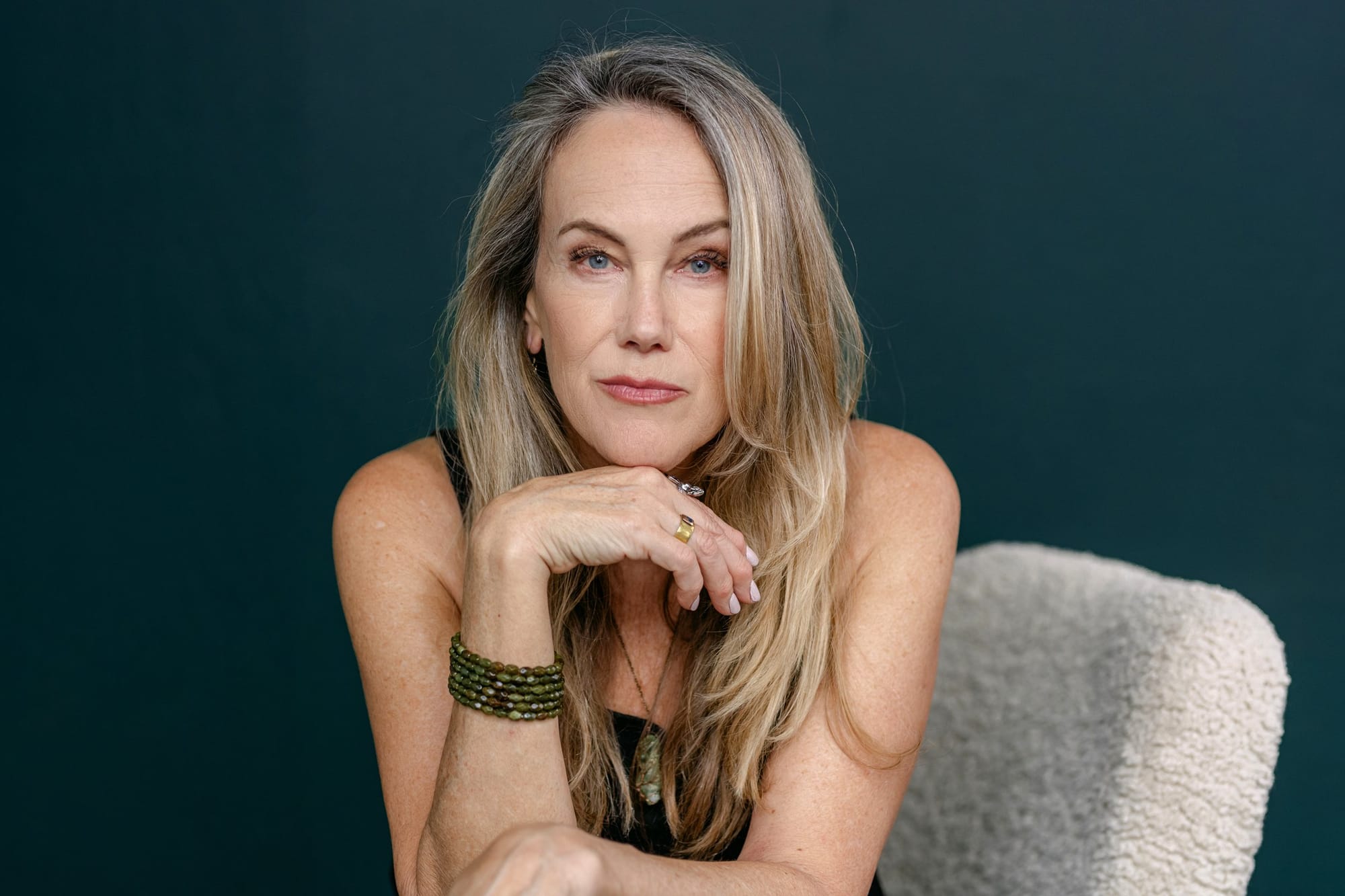 Moody portrait of a woman seated against a dark teal backdrop