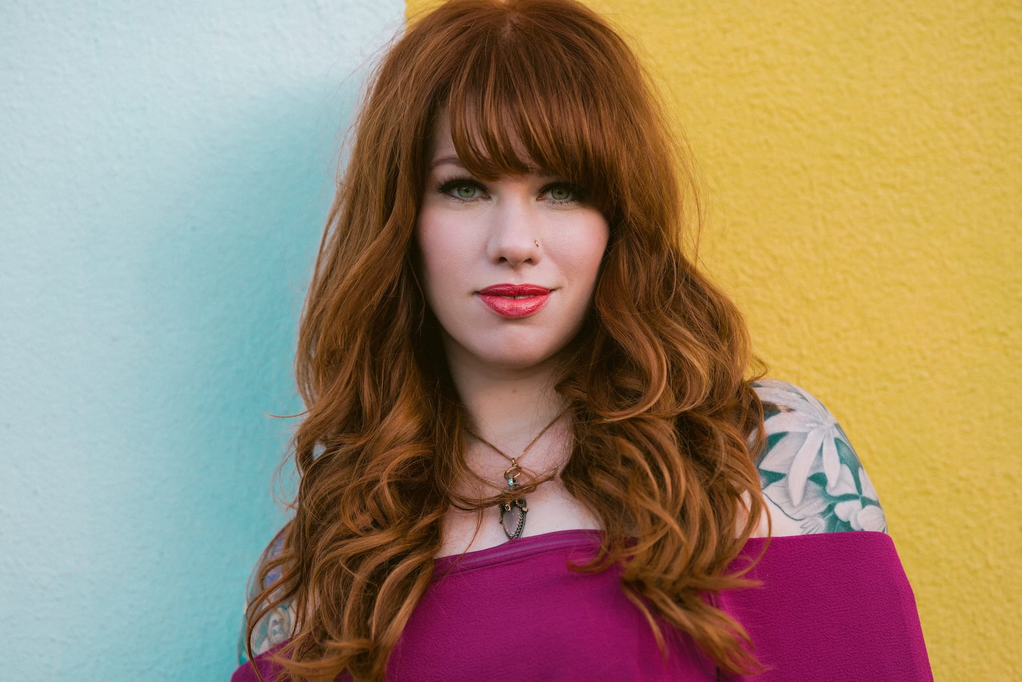 Redhead with bangs against a turquoise and yellow painted wall