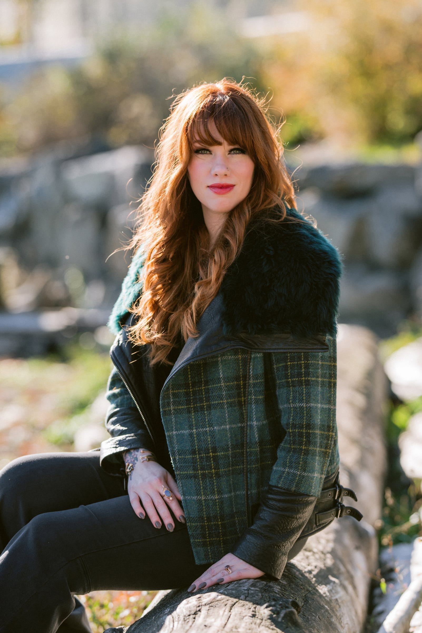 Redhead in a plaid coat seated outdoors among the rocks