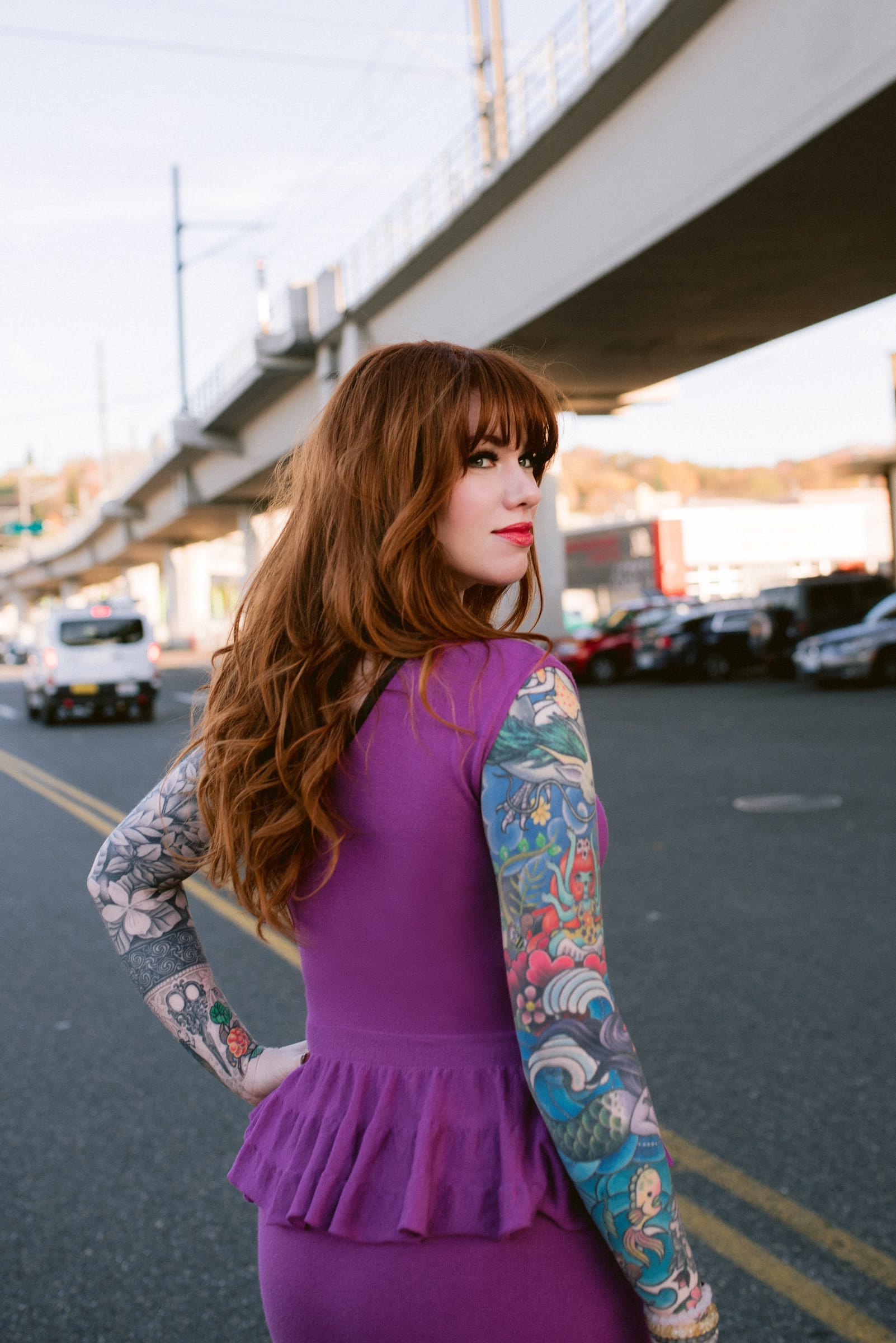 Tattooed woman in magenta glancing back on a city street