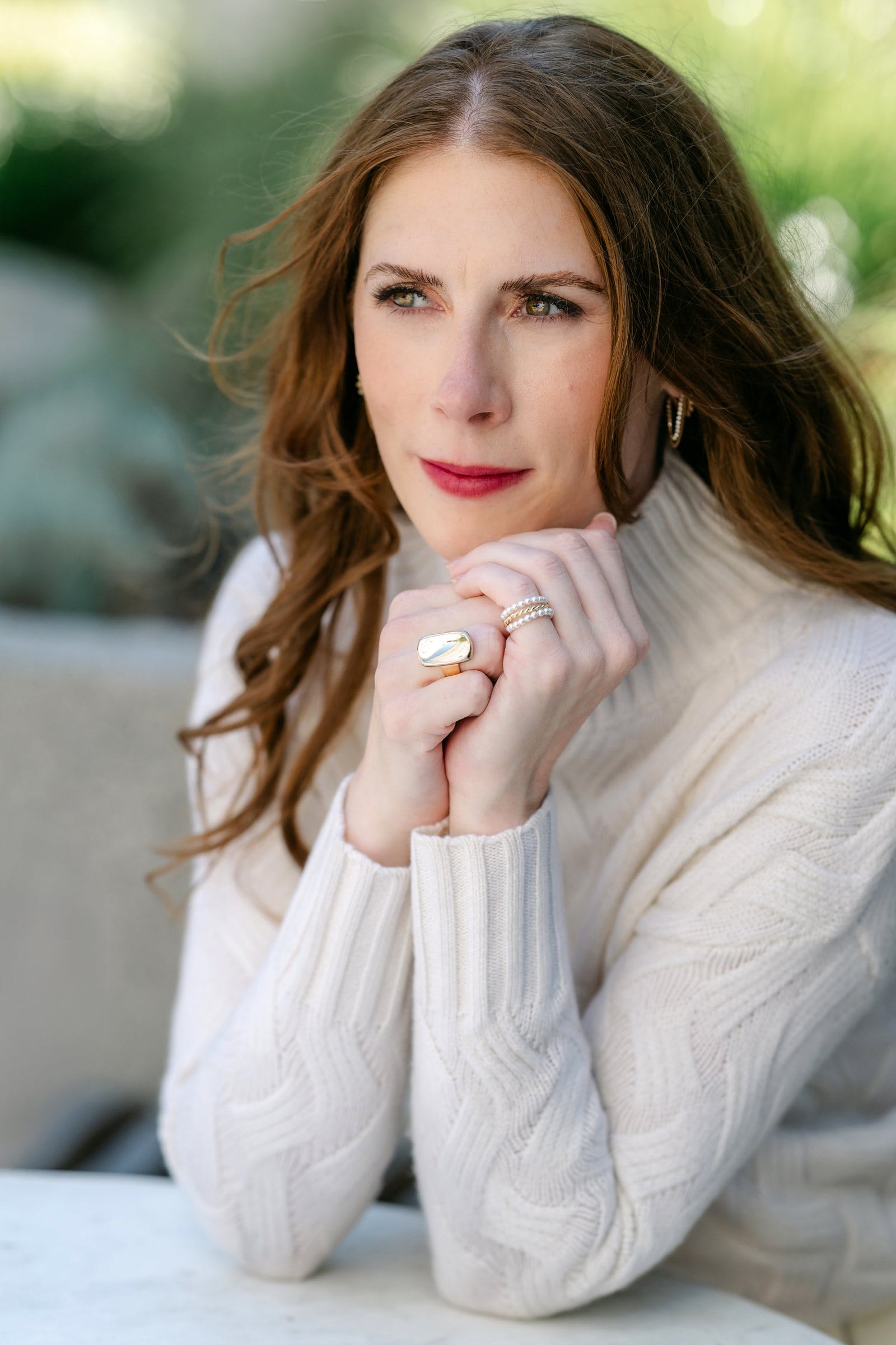 Thoughtful woman in a cream sweater with hands clasped at her chin
