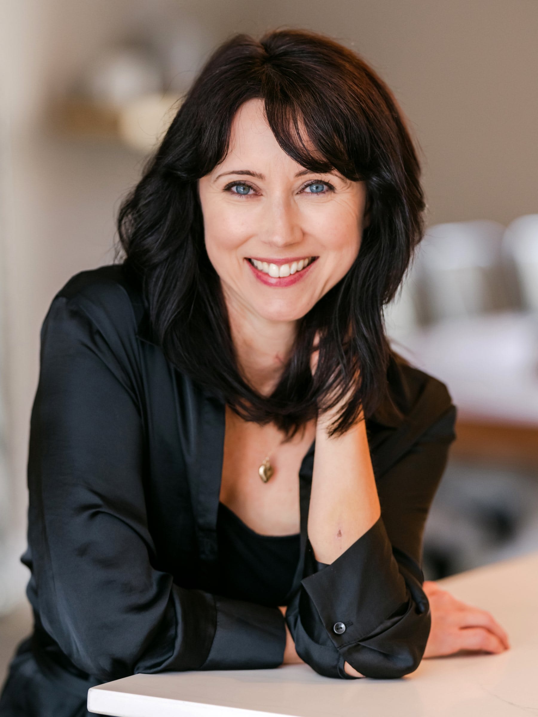 Dark-haired woman in a black silk blouse leaning on a table
